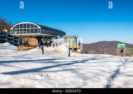 Wintergreen Resort, USA - March 2, 2025: People skiing at Dobie express ski chairlift, Blue Ridge mountains in background in winter snow Stock Photo