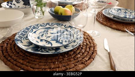 Blue White Ceramic Plates on Natural Woven Placemats. Sustainable table setting trend combines organic textures with traditional Mediterranean floral Stock Photo