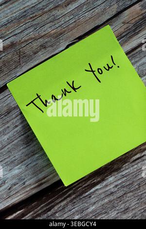 Vertical tilted image of one green sticky note that says Thank You, stuck on a wooden surface. Stock Photo