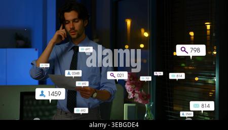 Holding phone, man in blue shirt, dark tie reading paper in night office with notification bubbles Stock Photo