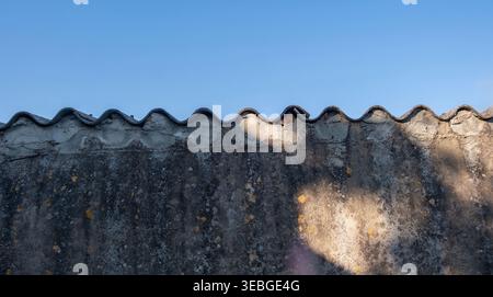 Old textured concrete wall with a wavy corrugated edge, closeup view. Blue sky background Stock Photo