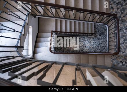 Top view of a geometric spiral staircase with marble steps and decorative patterned floor. Clean architectural composition with strong lines Stock Photo