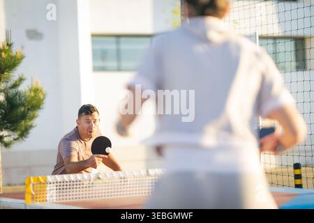 Focused middle-aged man playing outdoor table tennis match Stock Photo