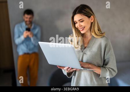Young happy multiethnic couple having fun while using laptop, digital device at home Stock Photo