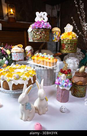 Vertical shot of ornate Easter cakes and ceramic bunnies on a white table. Stock Photo