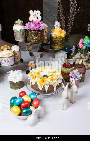Festive Easter still life with cakes, bright eggs, and porcelain bunnies. Stock Photo
