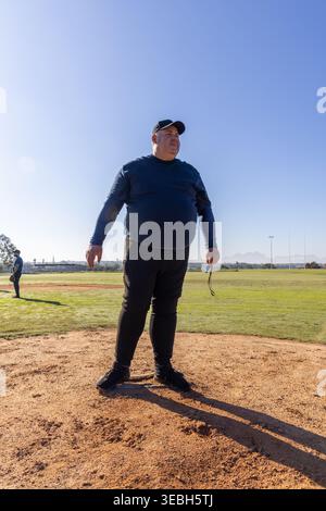 Senior man standing on raised pitcher's mound on diamond wearing baseball cap holding sunglasses Stock Photo