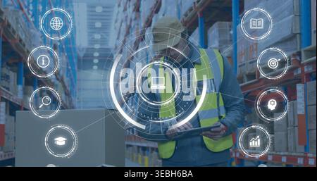 Using tablet, warehouse worker in yellow vest and cap updating stock near pallet racks with HUD Stock Photo