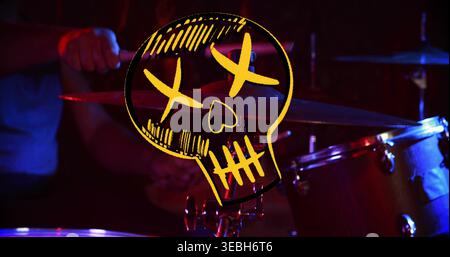 Showing yellow skull overlay hovering over drum kit on stage, drummer in short-sleeve blue shirt Stock Photo