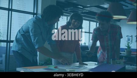 Leaning three coworkers examining papers on open-plan table, wearing red, blue, plaid shirts Stock Photo