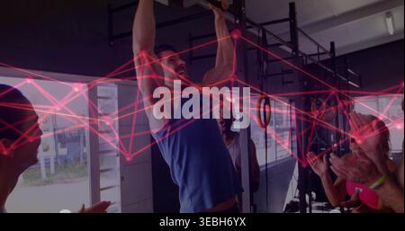 Pulling mid-adult man wearing blue sleeveless top doing pull-ups on metal rig at gym, red overlay Stock Photo