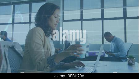 Working woman wearing beige blazer patterned top typing on laptop at open office holding to-go cup Stock Photo
