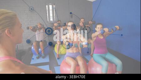 Leading coach guiding group raising weights on balls at studio, wearing activewear, network overlay Stock Photo