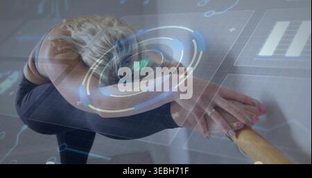 Stretching woman in black leggings and sports bra, balancing on barre in ballet studio HUD overlay Stock Photo