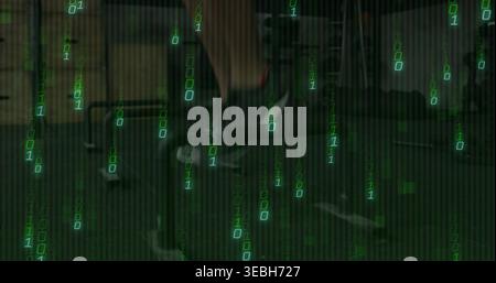 Typing tech wearing dark jacket in dim green office with desk monitors keyboard and binary code Stock Photo