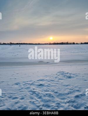 Golden sunrise over the frozen Dnipro river in Kyiv. Winter landscape with a bright sun rising over a vast, snow-covered frozen river. Stock Photo