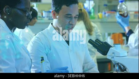 Operating male researcher using compound microscope at bench, wearing white lab coat, blue gloves Stock Photo
