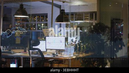 Displaying workstation with dual monitors showing code at nighttime office, with laptop and plant Stock Photo