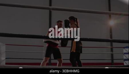 Training coach and black-tank boxer practicing punches in boxing ring, with mitts, gloves, ropes Stock Photo