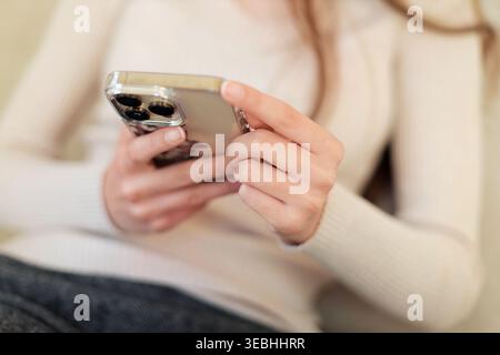 Woman using smartphone in cozy sweater. Close-up of hands holding a modern smartphone, suggesting texting, browsing, social media, or mobile Stock Photo