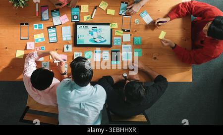 Programmer sharing Ux Ui design for mobile phone interface idea with software developer while designer writing idea at sticky notes. Start up team Stock Photo