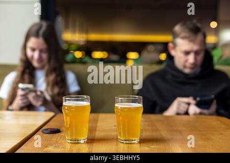 Couple distracted by phones in cafe. Two people sit apart using smartphones in a cafe, showing gadget addiction, emotional distance, and relationship Stock Photo