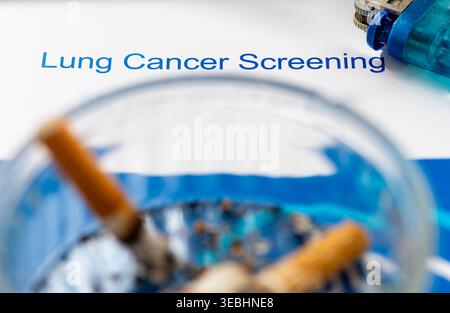A macro close up of a burning cigarette in an ashtray and a lighter on an information leaflet about lung cancer screening. Stock Photo