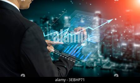 A business professional interacts with a high-tech interface displaying financial graphs, emphasizing growth and analysis in a modern urban setting Stock Photo
