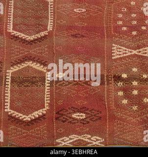 Handcrafted rug with repeating stylized geometric motifs in earthy reds, browns and off-white, woven texture showcasing traditional kilim-style crafts Stock Photo