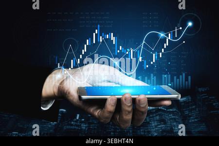A hand holding a smartphone displays glowing financial graphs and charts, representing data analytics in business. A visual concept for finance Stock Photo