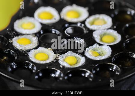 Documentary shot of fried quail eggs in a khanom krok pan at a Thai street market. Capturing the authentic sizzling texture of traditional snacks. Stock Photo