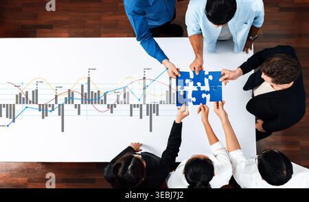 A diverse group of professionals collaborates on a business strategy. They analyze financial graphs while engaging with puzzle pieces, symbolizing Stock Photo