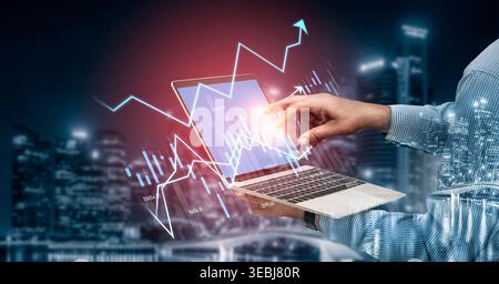 A hand interacts with a laptop displaying an abstract graph against an urban night skyline. This image represents technology and data analytics for Stock Photo
