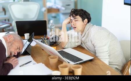 Tired male office workers having nap while sitting in workplace Stock Photo