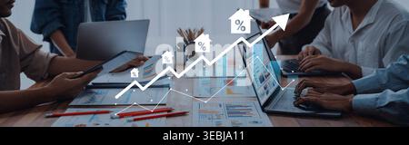A group of professionals engages in a detailed discussion about real estate market trends, analyzing data on laptops while using charts to visualize Stock Photo