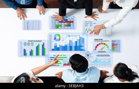 Collaborative Business Team Analyzing Data Trends and Statistics on Table During Meeting with Graphs and Charts Displayed on Screens Quark. Stock Photo