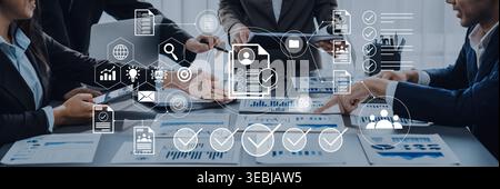 A focused group of business professionals collaborates in a modern office, analyzing charts and discussing project strategies using digital devices Stock Photo