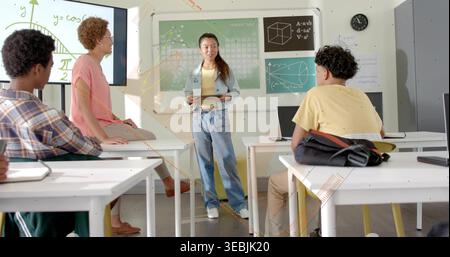 Teaching instructor holding tablet and explaining cosine graph on display in classroom with laptops Stock Photo