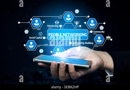 A hand holding a smartphone displays a conceptual image of people networking with digital icons, representing mentorship, community, and building Stock Photo