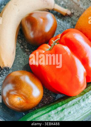 Close-up of fresh vegetables and fruits including red bell pepper, cucumber, tomatoes, and banana on a textured surface. Vibrant colors and natural li Stock Photo