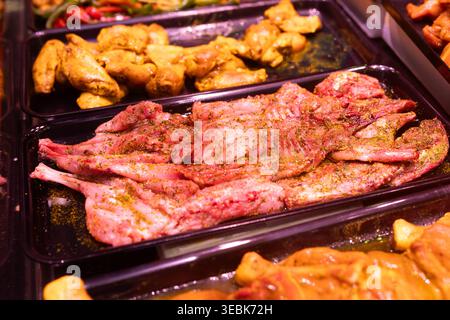 Marinated rabbit, halves, quarters are presented in the display case. The butcher's shop sells fresh meat products, semi finished products Stock Photo