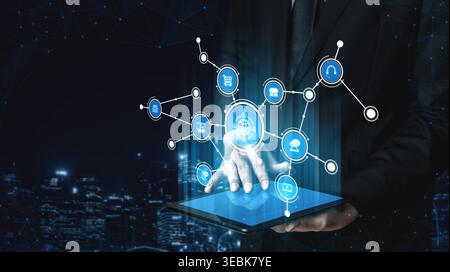 A businessman interacts with a high-tech tablet displaying a network of icons and digital connections, symbolizing modern technology and business Stock Photo