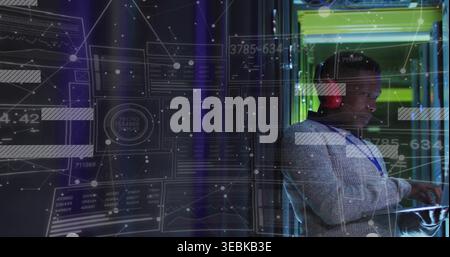Monitoring technician wearing gray sweater and lanyard using laptop at server rack, HUD, copy space Stock Photo