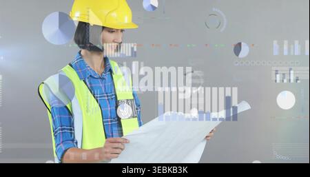 Reviewing engineer in yellow hard hat, neon vest, holding plan against gray backdrop with AR charts Stock Photo