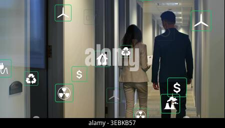 Walking two coworkers in suits reading tablet in office corridor, seeing floating graphic icons Stock Photo