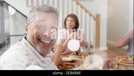 Smiling mature man in striped shirt sitting at home table, showing plates salad bottles glass Stock Photo