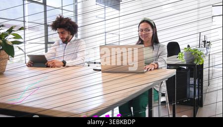 Working Middle Eastern man and Chinese woman in business clothes using tablet and laptop at table Stock Photo