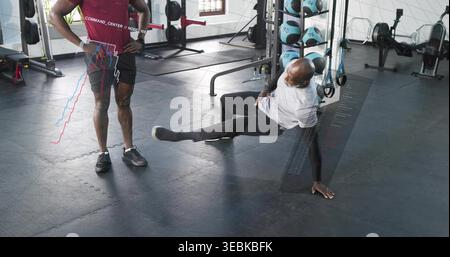 Coaching trainer in maroon shirt guiding client doing single-leg move at gym, with digital overlay Stock Photo