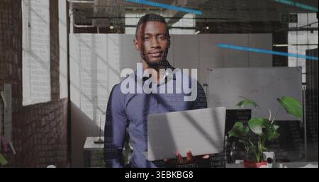 Holding silver laptop, man in dark blue shirt and trousers standing in office, code reflecting Stock Photo