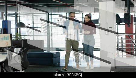 Walking pair discussing project in modern workspace, casually dressed with monitor charts on glass Stock Photo